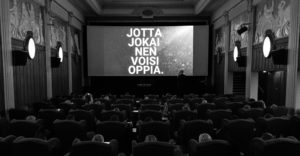 Valkokankaalla eOppivan slogan Jotta jokainen voisi oppia. Yleisö odottaa taahtuman alkamista. 