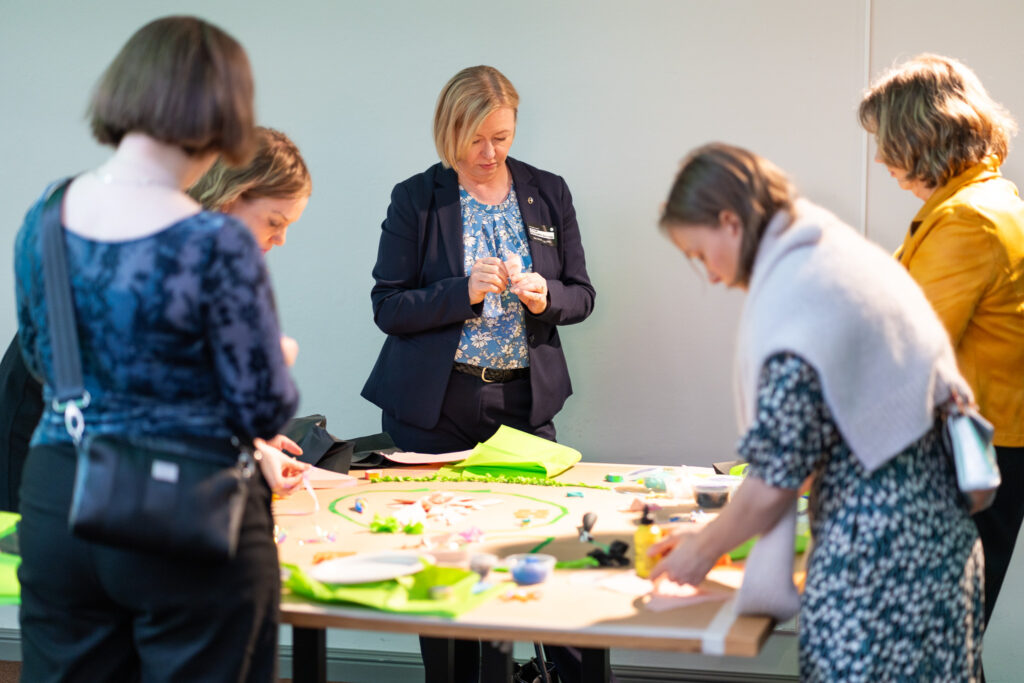 Ihmiset luovat yhdessä tilataideteosta ison pöydän ympärillä eOppiva-gaalassa.